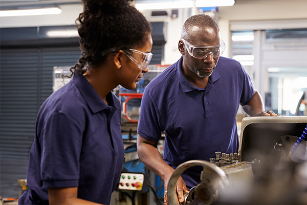 Two people wearing safety glasses while using a machine